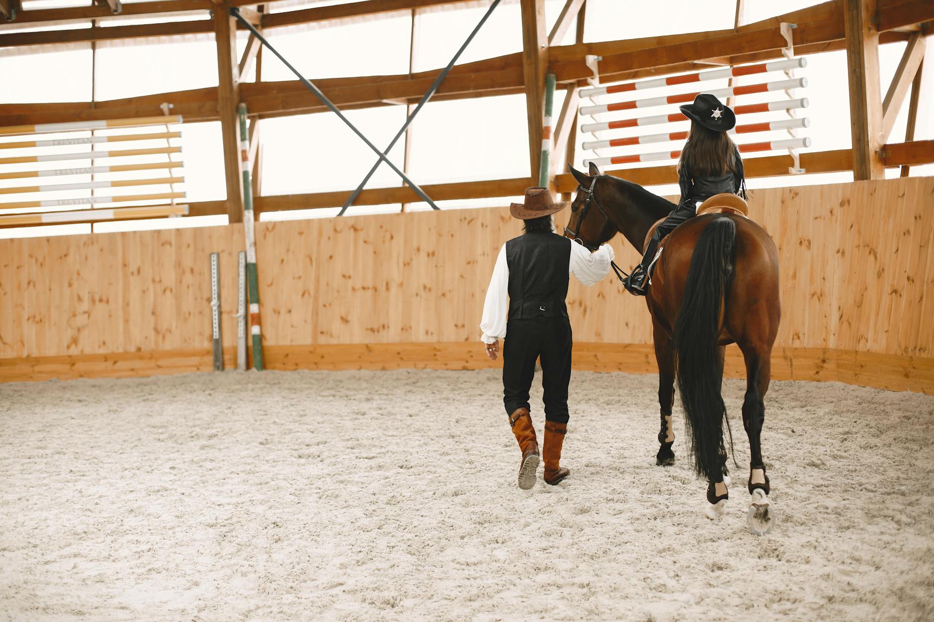 Instruktor prowadzi dziewczynę na koniu w krytej ujeżdżalni