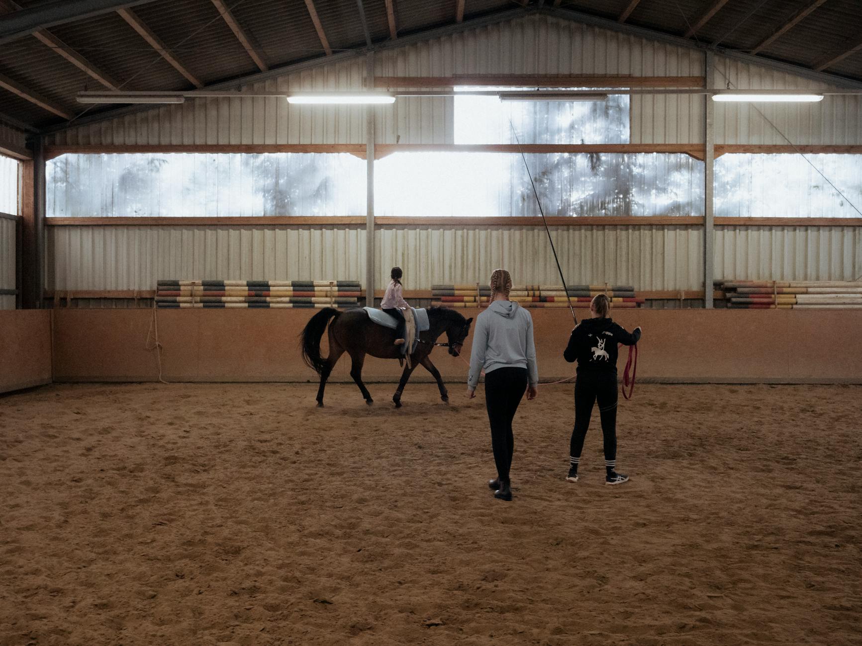 Instruktorka uczy młodą dziewczynkę jazdy konnej w hali