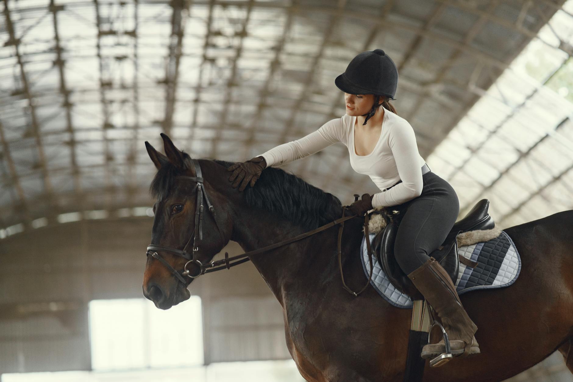 Kobieta w legginsach jeździeckich trenuje na koniu w krytej hali