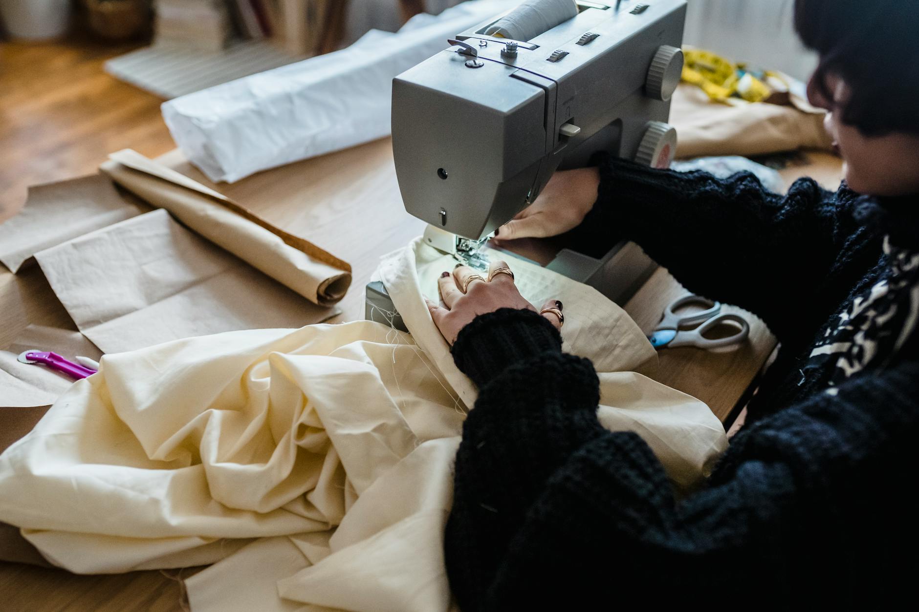 Kobieta w swetrze szyje materiał na maszynie w pracowni krawieckiej