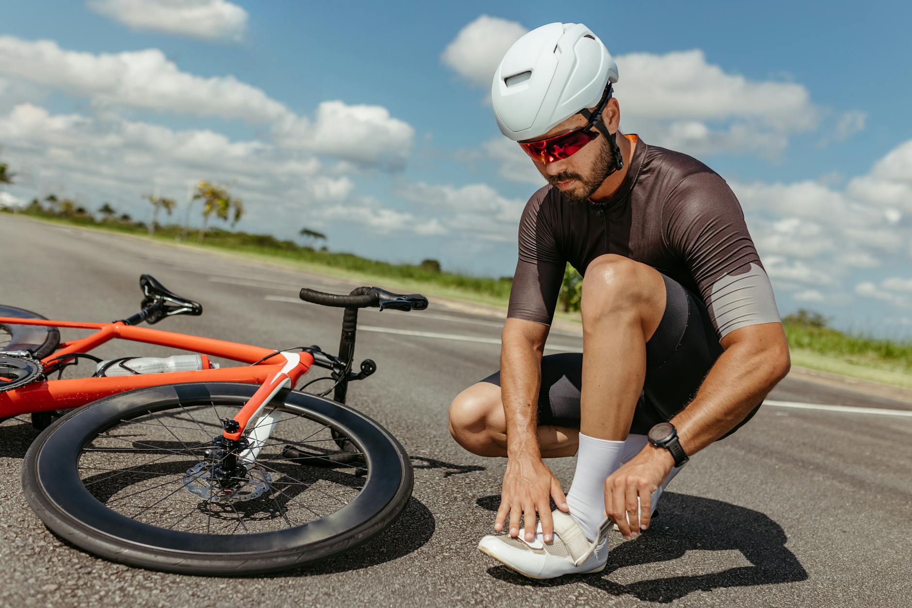 Rowerzysta przy rowerze poprawia buty kolarskie na tle błękitnego nieba